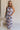 Full body view of female model wearing the Emily Black Multi Geometric Halter Maxi Dress which features Black, Blue, Orange, Pink and White Lightweight Fabric, Geometric Pattern, Maxi Length, White Thigh Length Lining, Ruffle Hem and Halter Neckline with Back Tie Strap