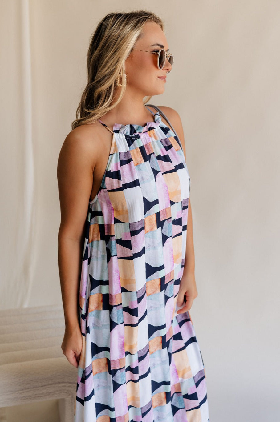 Side view of female model wearing the Emily Black Multi Geometric Halter Maxi Dress which features Black, Blue, Orange, Pink and White Lightweight Fabric, Geometric Pattern, Maxi Length, White Thigh Length Lining, Ruffle Hem and Halter Neckline with Back Tie Strap