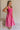 Full body side view of female model wearing the Cecilia Pink Smocked Midi Dress which features Pink Lightweight Fabric, Pink Lining, Pockets On Each Side, Midi Length, Textured Upper, Square Neckline and Sleeveless