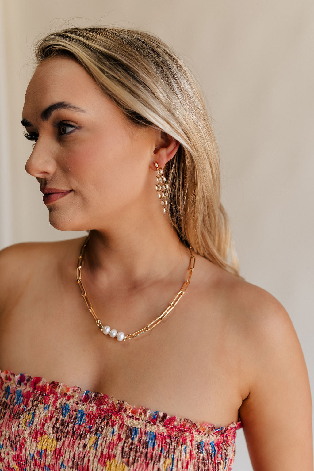 Close up side view of female model wearing the Gracie Pearl & Gold Dangle Earring which features pearls set in gold, dangle pearls linked together and back closure