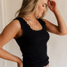 Side view of female model wearing the Myla Black Ruffle Sleeveless Tank which features Black Knit Fabric, Lettuce Hem Details, Round Neckline and Sleeveless