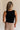 Back view of female model wearing the Myla Black Ruffle Sleeveless Tank which features Black Knit Fabric, Lettuce Hem Details, Round Neckline and Sleeveless