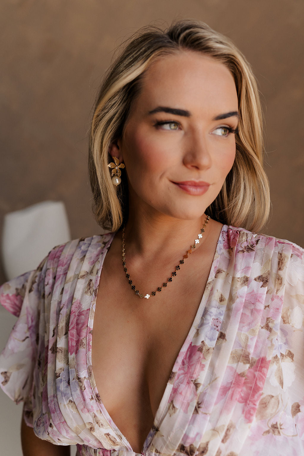 Clos eup view of female model wearing the Mina Gold Floral & Pearl Dangle Earring which features gold flower shaped stud linked with a pearl dangle medallion