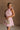 Upper body front view of female model wearing the Eva Pink Sheer Tie Back Mini Dress that has pink sheer fabric with pink lining and a halter neck with a bow tie back