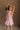 Back view of female model wearing the Eva Pink Sheer Tie Back Mini Dress that has pink sheer fabric with pink lining and a halter neck with a bow tie back