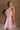 Upper body front view of female model wearing the Eva Pink Sheer Tie Back Mini Dress that has pink sheer fabric with pink lining and a halter neck with a bow tie back