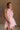 Upper body front view of female model wearing the Eva Pink Sheer Tie Back Mini Dress that has pink sheer fabric with pink lining and a halter neck with a bow tie back