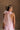 Upper body back view of female model wearing the Eva Pink Sheer Tie Back Mini Dress that has pink sheer fabric with pink lining and a halter neck with a bow tie back