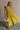 Full body front view of female model wearing the Kristina Chartreuse Smocked Sleeveless Midi Dress that has chartreuse fabric with a smocked upper, ruffle straps, and a midi length hem.