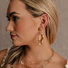 Side view of model's face; model is wearing the Nyomi Raffia & Gold Earrings that have ivory and tan raffia intertwined with gold metal into a circle hanging from tan raffia ball.