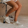 Side view of female model wearing the Alta Sneaker in Off White which features light grey and white suede upper fabric, white sole, and lace up details
