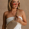 Front view of female model the Paige Tan & Black Sling Bag across her chest. It has tan and black woven fabric, a zipper, and a tan strap.
