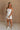 Full body front view of female model wearing the Kelsey White Denim Romper that has white denim fabric, a strapless neck, and a pleated skirt over shorts lining.