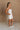 Full body side view of female model wearing the Kelsey White Denim Romper that has white denim fabric, a strapless neck, and a pleated skirt over shorts lining.