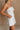 Close Upper body side view of female model wearing the Kelsey White Denim Romper that has white denim fabric, a strapless neck, and a pleated skirt over shorts lining.