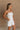 Upper body side view of female model wearing the Kelsey White Denim Romper that has white denim fabric, a strapless neck, and a pleated skirt over shorts lining.