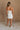 Full body back view of female model wearing the Kelsey White Denim Romper that has white denim fabric, a strapless neck, and a pleated skirt over shorts lining.