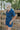 Frontal side view of female model wearing the Mavis Denim Short Sleeve Zip-Up Romper in Medium Wash which features Denim Fabric, Two Front Pockets, Front Zipper Closure, Adjustable Monochrome Belt with Loops, Collared Neckline and Short Sleeves