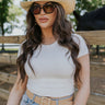 Upper body front view of brunette model wearing the Kira Short Sleeve Cropped Top in ivory that has ivory fabric, short sleeves, a round neck, and cropped waist. Worn with jeans and belt.