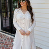 Full body front view of female model wearing the Everly White Button Up Midi Dress that has white fabric, long sleeves, a button up front, collar, chest pockets, and a frayed high-low hemline with back slit.