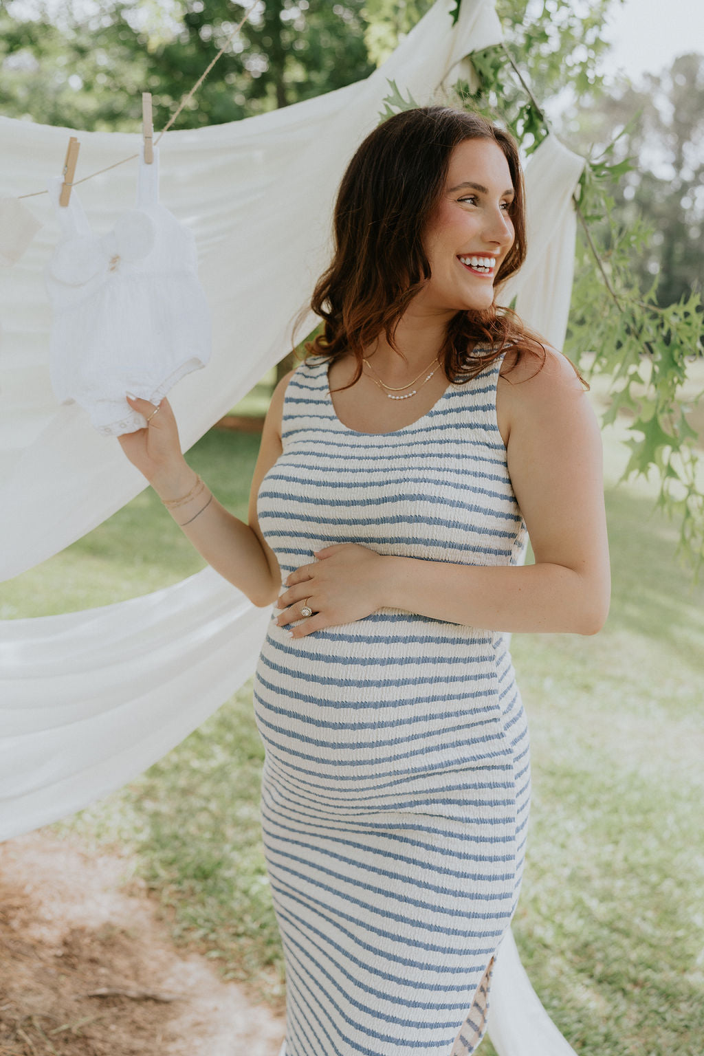 front view of female model wearing the Casey Cream & Blue Striped Midi Dress that has cream and blue horizontal stripes, bodycon fit, thick straps, a side slit, and round neck.