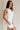 side view of female model wearing the Taylor Off White Bow Cut-Out Mini Dress which features White Lightweight Fabric, White Lining, Mini Length, Square Neckline, Side Zipper with Hook Closure and Bow Cut-Out Back Detail