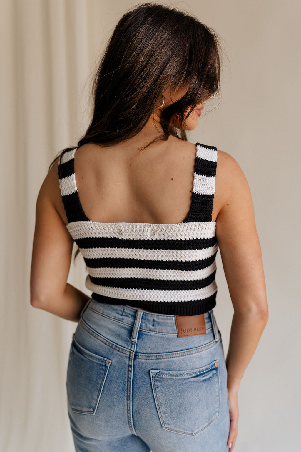 back view of female model wearing the Kai Black & White Stripe Knit Tank which features Black and White Crochet Knit, Stripe Pattern, Cropped Waist, Rhinestone Button Up, Square Neckline and Sleeveless