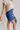 Close side view of model wearing the Mara Blue High Waist Shorts that have blue fabric, a high-rise elastic back waist. Worn with beige top.