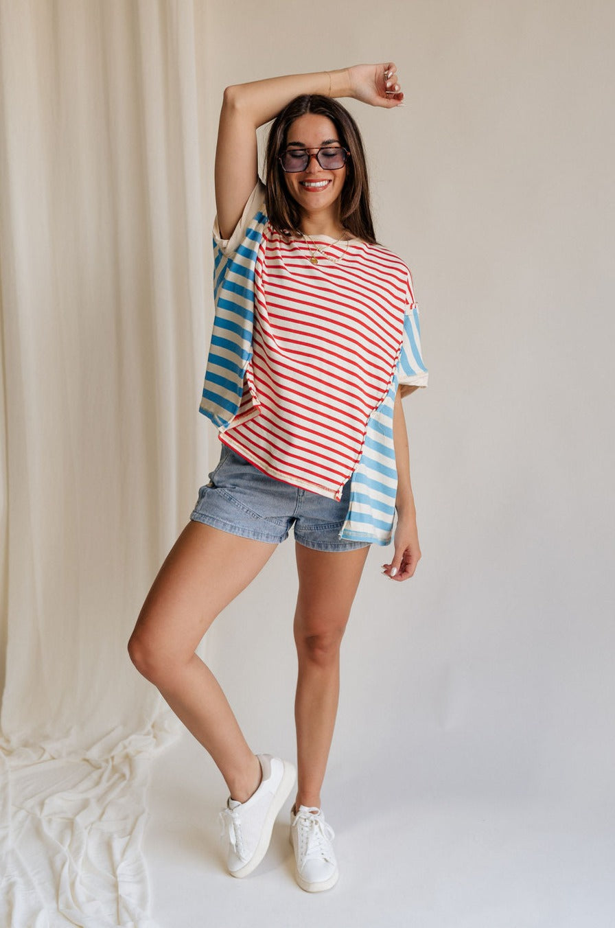 Full body front view of female model wearing the Abigail Red, Cream, & Blue Striped Top that has a red striped center, blue striped sides, a round neck, short sleeves, and oversize fit.