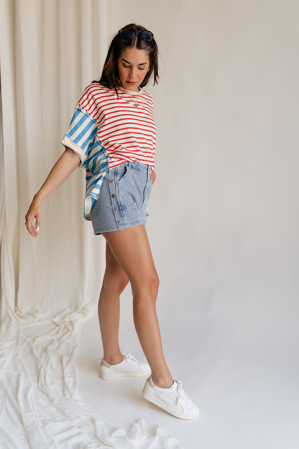 Full body side view of female model wearing the Hailey Silver Stud Denim Shorts that have light wash denim, silver stud details, pockets, and a front zipper.