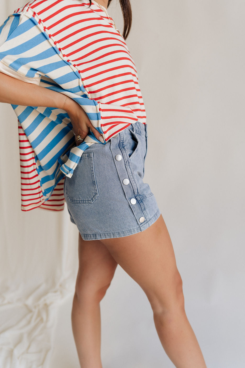 Close side view of female model wearing the Hailey Silver Stud Denim Shorts that have light wash denim, silver stud details, pockets, and a front zipper.