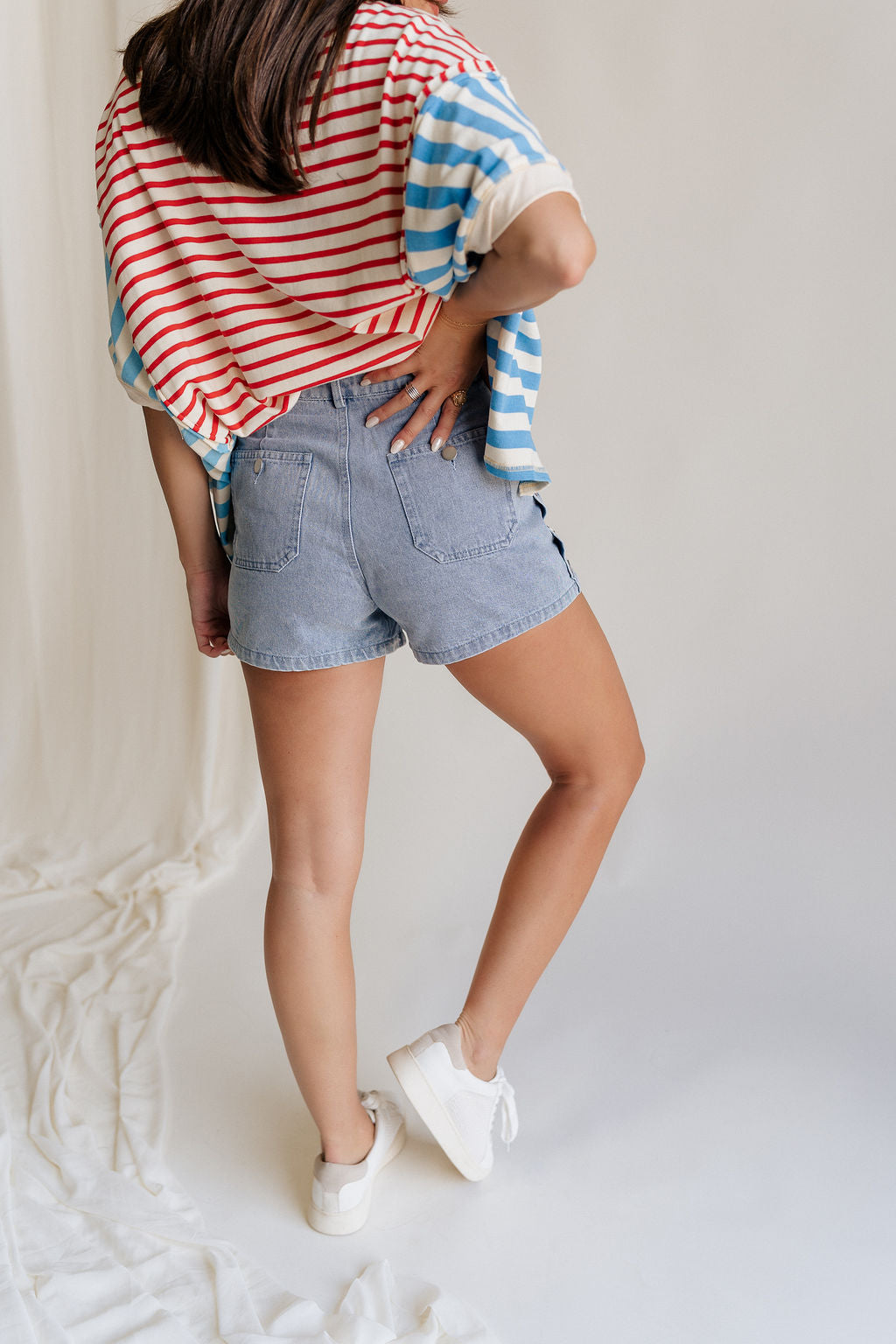Back view of female model wearing the Hailey Silver Stud Denim Shorts that have light wash denim, silver stud details, pockets, and a front zipper.