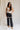 Full body front view of female model wearing the Remi Rhinestone Slit Black Jeans that have black denim, thigh slits with rhinestone trim, and pockets.
