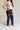 Lower body side view of female model wearing the Remi Rhinestone Slit Black Jeans that have black denim, thigh slits with rhinestone trim, and pockets.