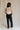 Full body back view of female model wearing the Remi Rhinestone Slit Black Jeans that have black denim, thigh slits with rhinestone trim, and pockets.