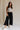 Full body front view of female model wearing the Meredith Black Cropped Wide Leg Pants that have black fabric, cropped wide legs, side slits, and a drawstring waist.