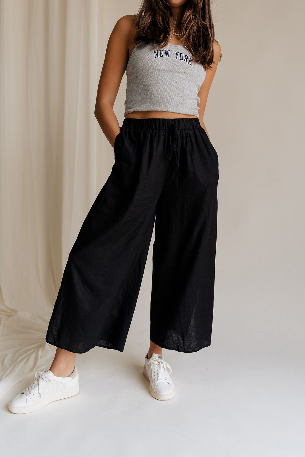 Lower body front view of female model wearing the Meredith Black Cropped Wide Leg Pants that have black fabric, cropped wide legs, side slits, and a drawstring waist.