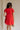 Back view of female model wearing the Nalani Tiered Short Sleeve Mini Dress in Red that has red fabric, a tiered mini length body, v neck, and short sleeves.