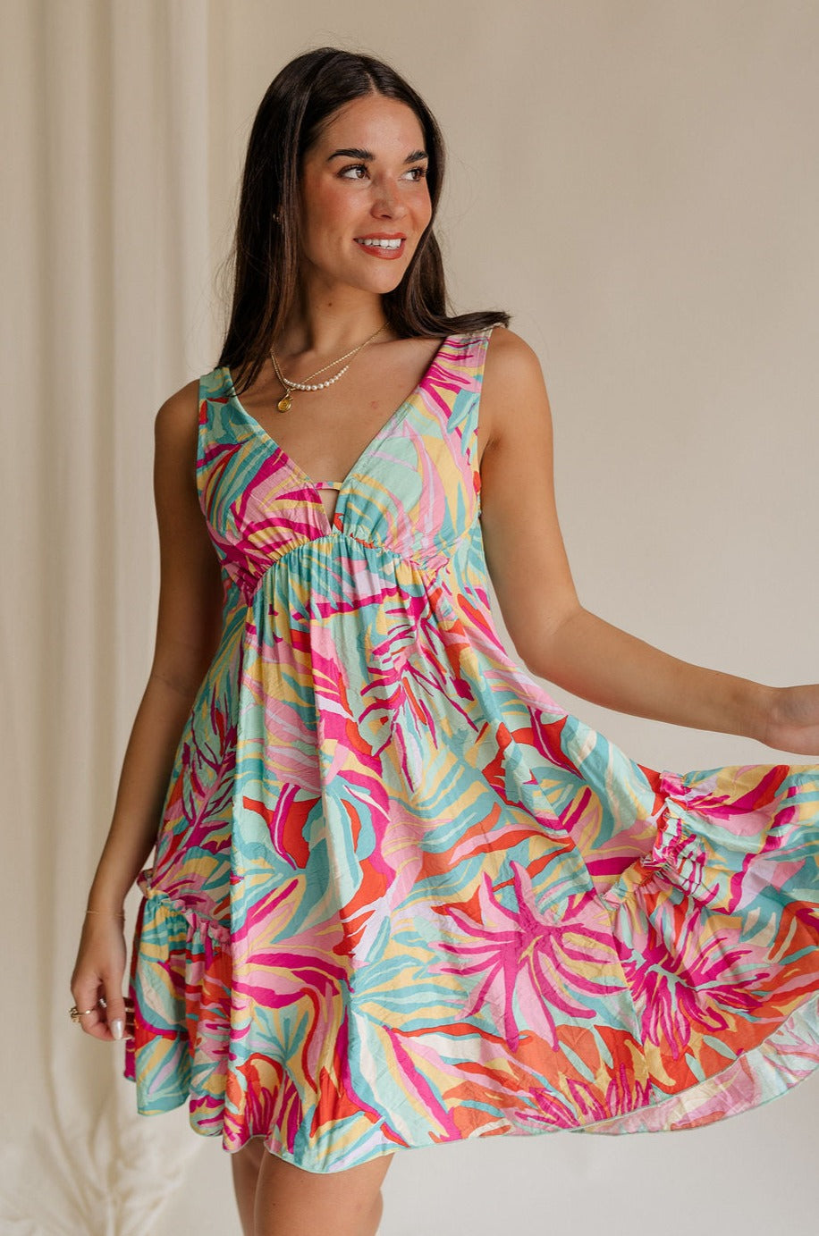 Front view of female model wearing the Florence Floral Print Sleeveless Mini Dress that has a colorful floral palm print, v neck and back, and mini length.