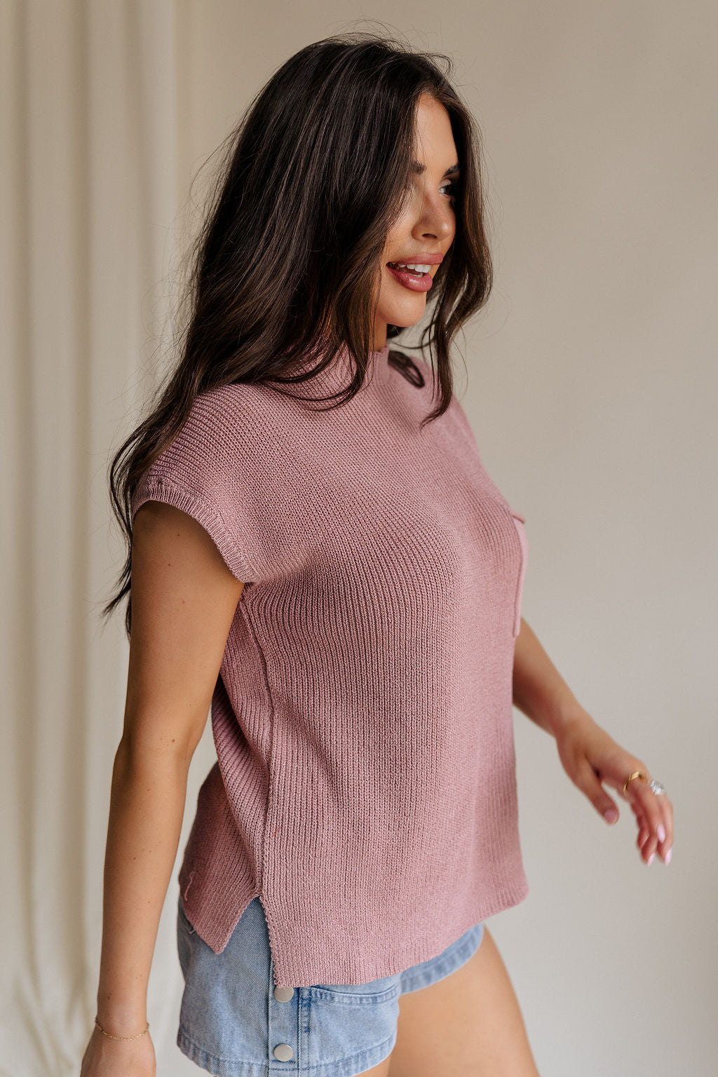 side view of female model wearing the Arana Knit Short Sleeve Top which features Lightweight Knit Fabric, Slight Slit Details, Front Left Chest Pocket, Round Neckline and Short Sleeves. the top is available in beige and mauve