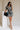 Full body front view of model wearing the Melanie Black & Cream Printed Romper that has black and cream fabric with a swirl print, a button up front, collar, tie belt, and short sleeves.