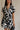 Close-up front view of model wearing the Melanie Black & Cream Printed Romper that has black and cream fabric with a swirl print, a button up front, collar, tie belt, and short sleeves.