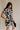 Frontal side view of model wearing the Melanie Black & Cream Printed Romper that has black and cream fabric with a swirl print, a button up front, collar, tie belt, and short sleeves.