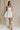 Full body front view of female model wearing the Sasha Off White Tie Strap Mini Dress that has cream fabric with rosette florals, cream tie straps, a straight neckline, and fit and flare style.
