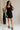 Full body view of female model wearing the Thea Black Square Neckline Mini Dress which features Black Linen Fabric, Black Lining, Mini Length, Side Pockets, Square Neckline, Sleeveless and Monochrome Back Zipper with Hook Closure