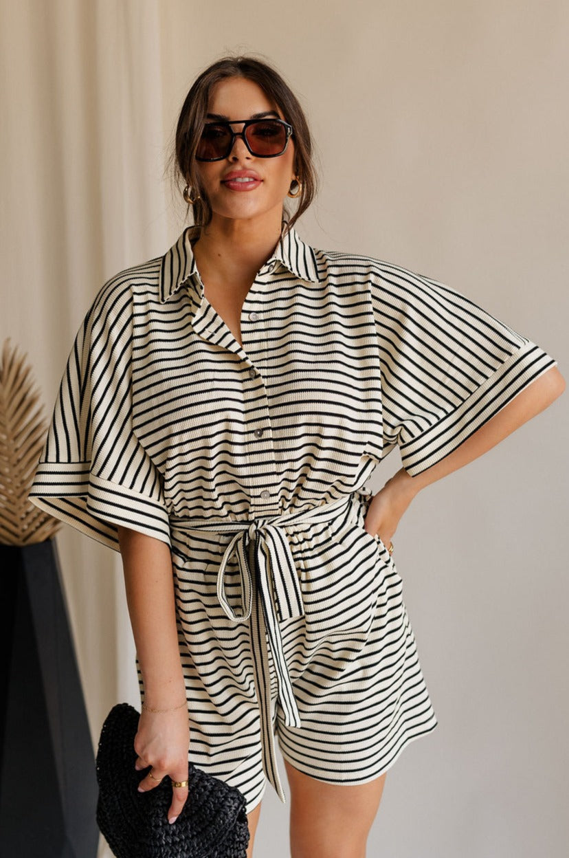 front view of female model wearing the Eden Black & Cream Stripe Tie Romper which features Black and Cream Stripe Lightweight Fabric, Mini Length, Side Pockets, Front Button Up Closure, Collared Neckline, Short Sleeves and Waistband Tie Straps