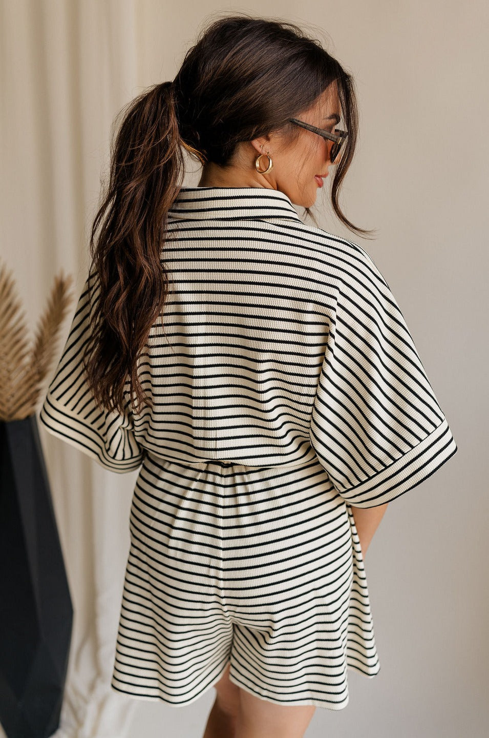 back view of female model wearing the Eden Black & Cream Stripe Tie Romper which features Black and Cream Stripe Lightweight Fabric, Mini Length, Side Pockets, Front Button Up Closure, Collared Neckline, Short Sleeves and Waistband Tie Straps