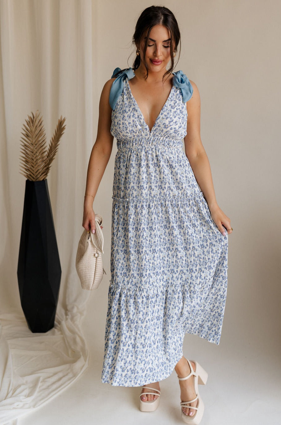 Full body view of female model wearing the Palmer Ivory & Blue Floral Tie Straps Midi Dress which features Light Blue and White Floral Print, Plisse Textured Fabric, White Lining, Tiered Body, Midi Length, Plunge Neckline and Blue Tie Straps