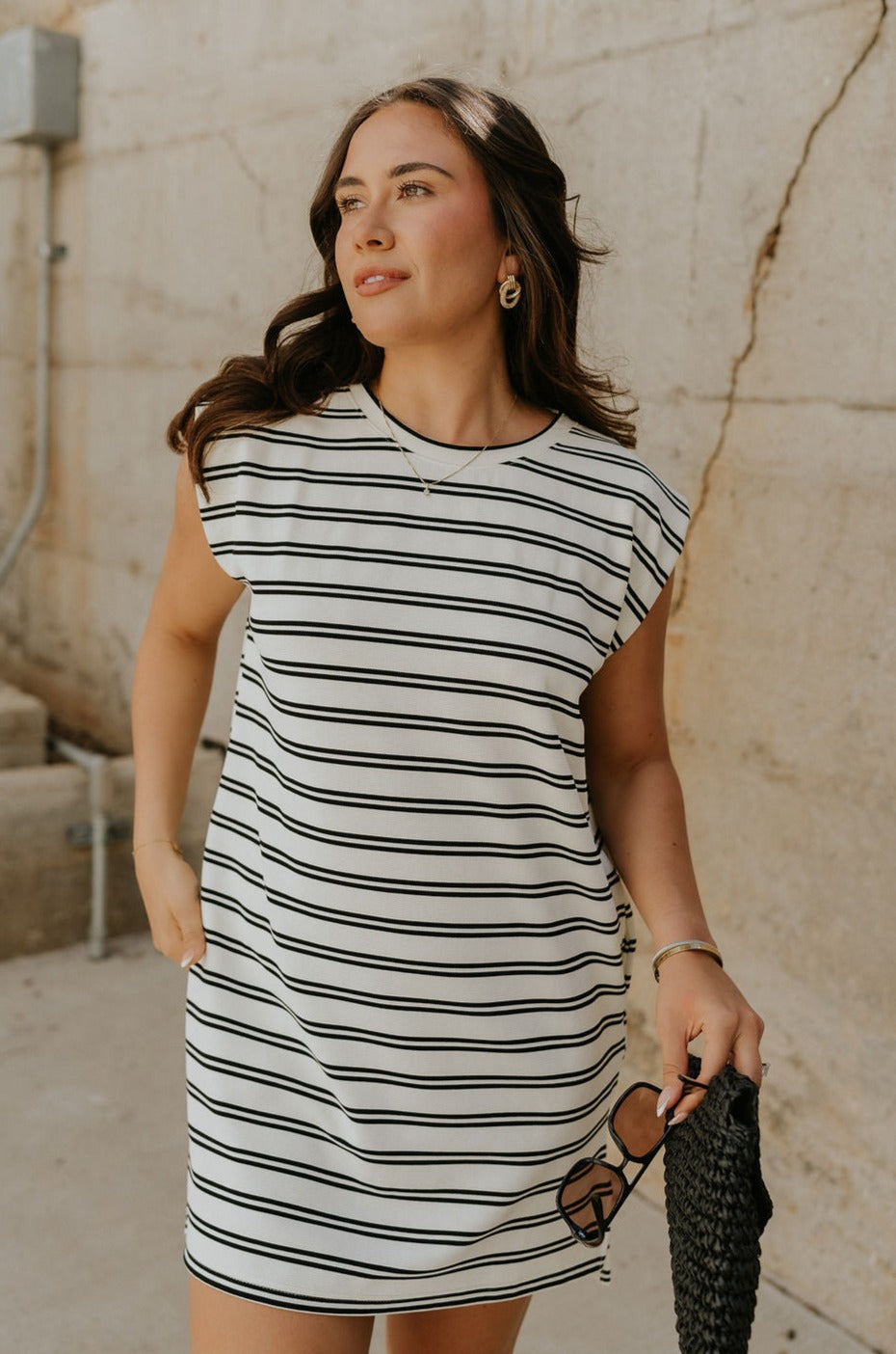 Upper body front view of model wearing the Gabriella Cream & Black Striped Mini Dress that has cream fabric with horizontal black stripes, a sleeveless body, round neck, and side pockets.