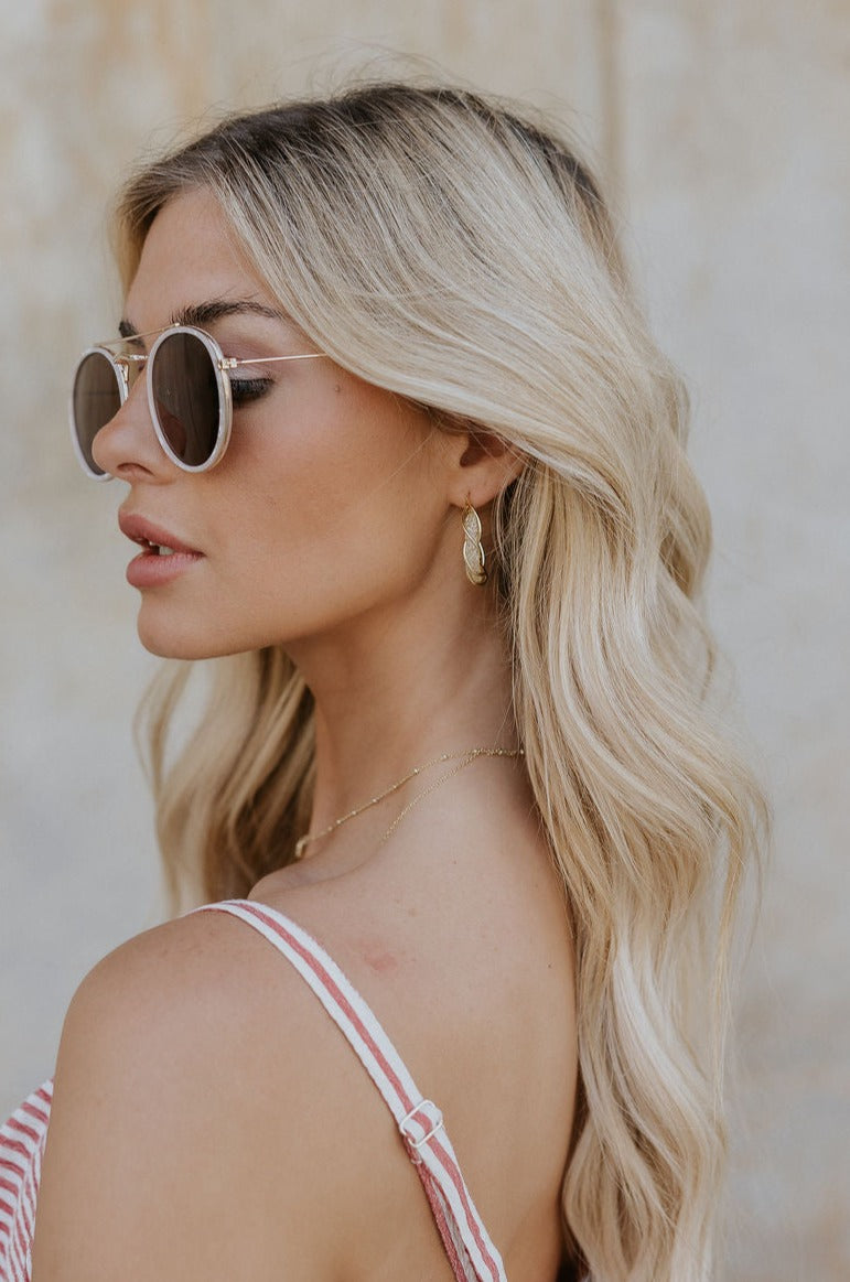 Side view of model's face; model is wearing the Nadia Twisted Gold Hoop Earrings that feature gold metal twisted around a clear interior hoop.